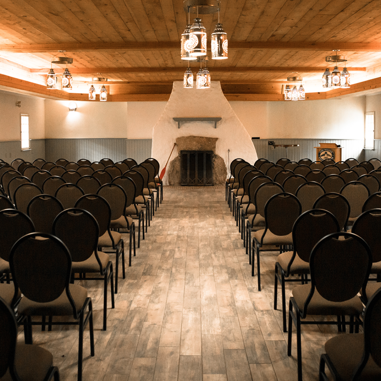 the Canot du Nord (North Canoe Shed) set up for a meeting with a center aisle and chairs in rows on either side facing a fireplace and podium