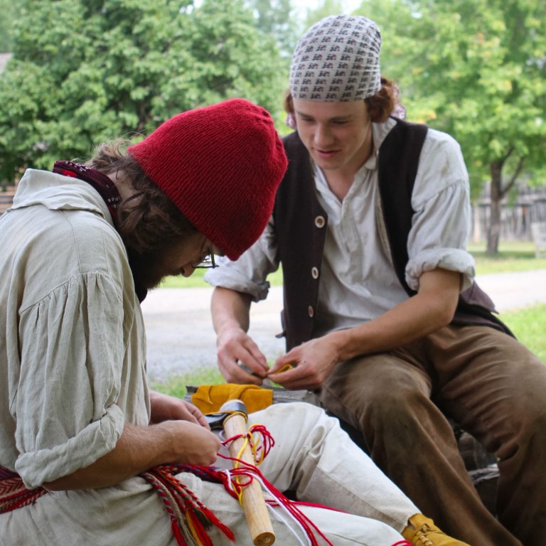 Two Historic Interpreters doing historic crafts of weaving and sewing leather